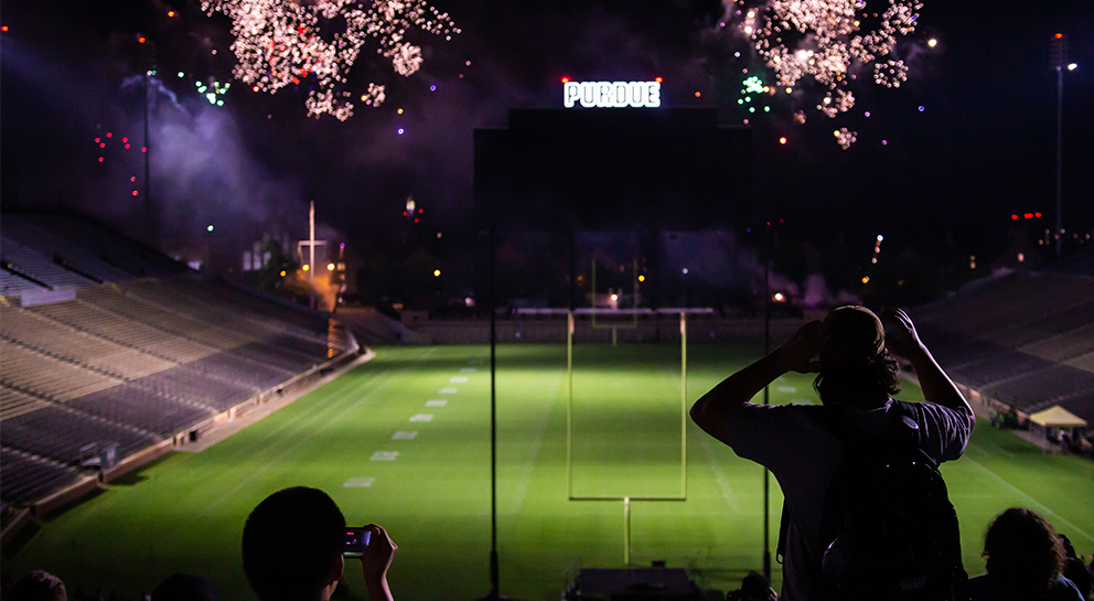 a student at Ross-Ade stadium at night watching a fireworks display