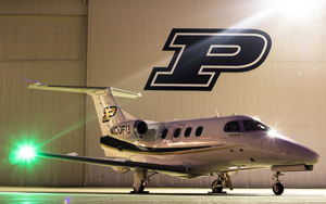 Photo of a Purdue plane in the hanger with the Purdue logo on the wall behind it