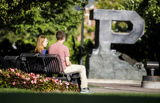 students sitting on a bench in the sun in front of the Purdue P statue