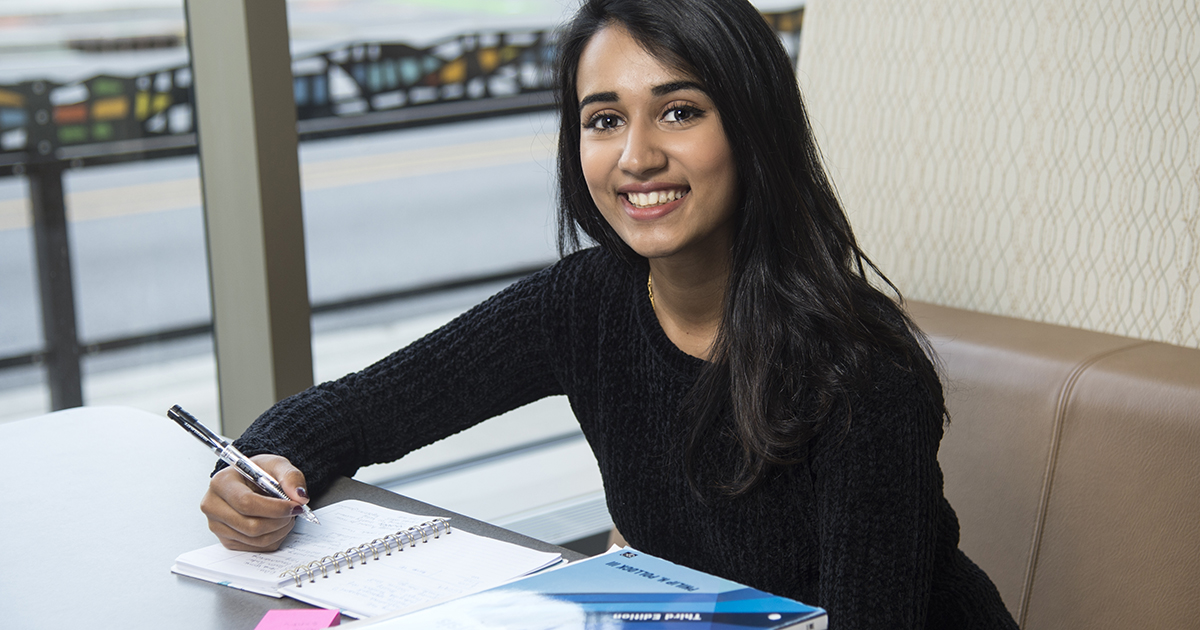 A student sits in a booth writing in a notebook