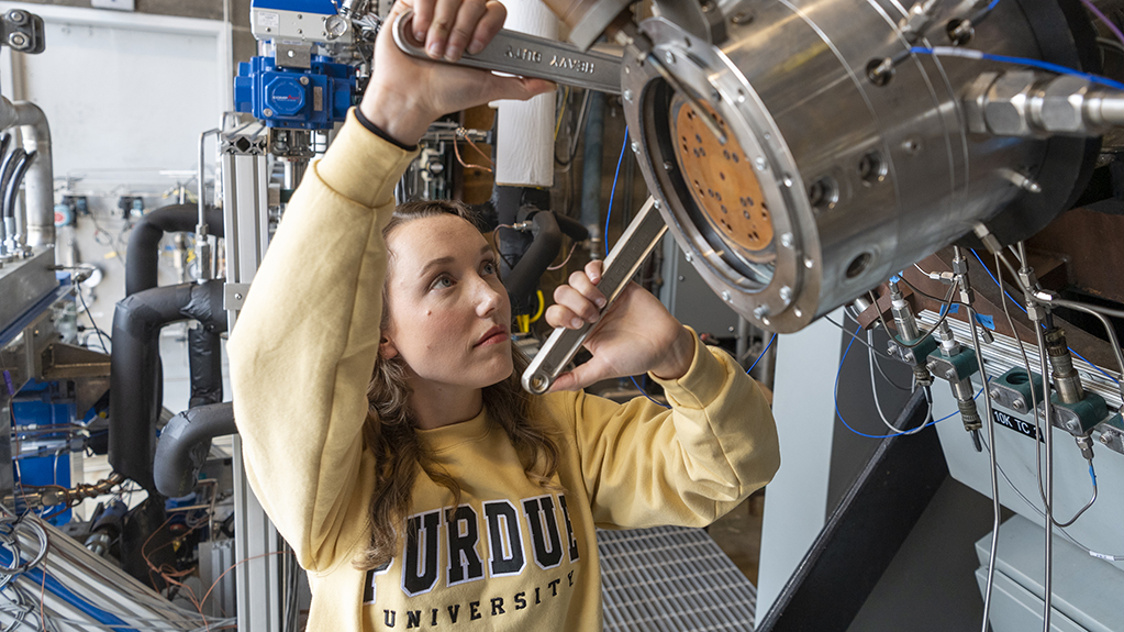 A student uses tools to tighten equipment in the Zucrow Lab