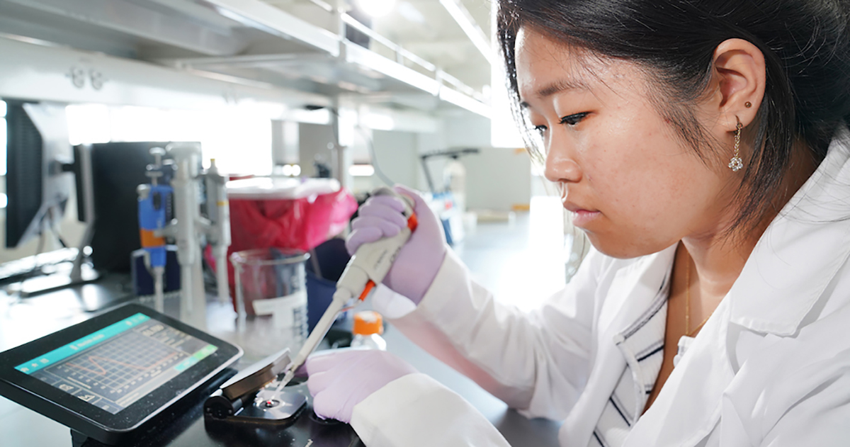 Young woman in lab coat pipetting into device