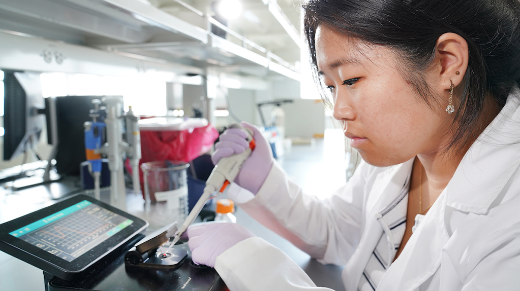 Young woman in lab coat pipetting into device