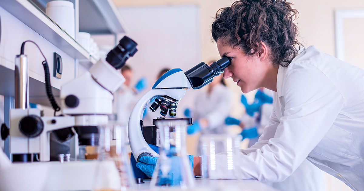A student looks into a microscope in a lab