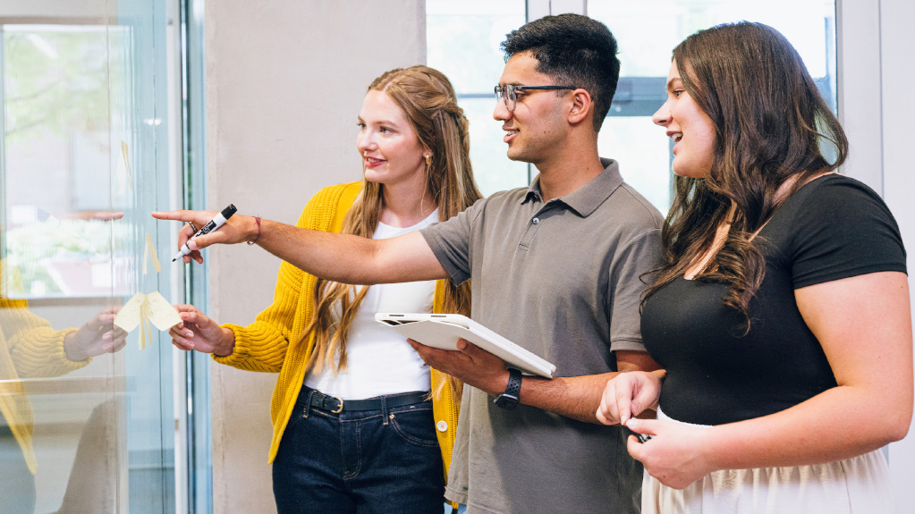 Finance students pointing to and discussing numbers on a board