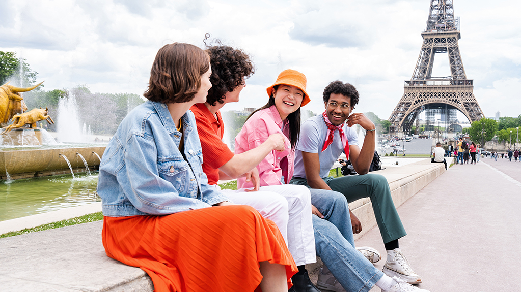 Students sit on a wall along the sidewalk with the Eiffel tower in the background