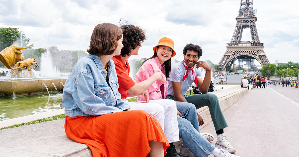Students sit on a wall along the sidewalk with the Eiffel tower in the background