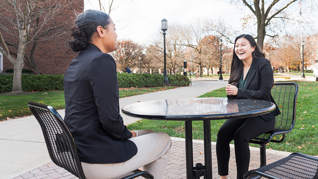 Two girls in suits talking and smiling at a table