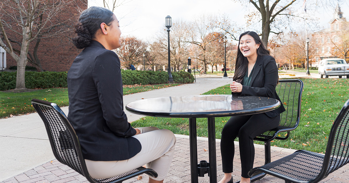 Two girls in suits talking and smiling at a table