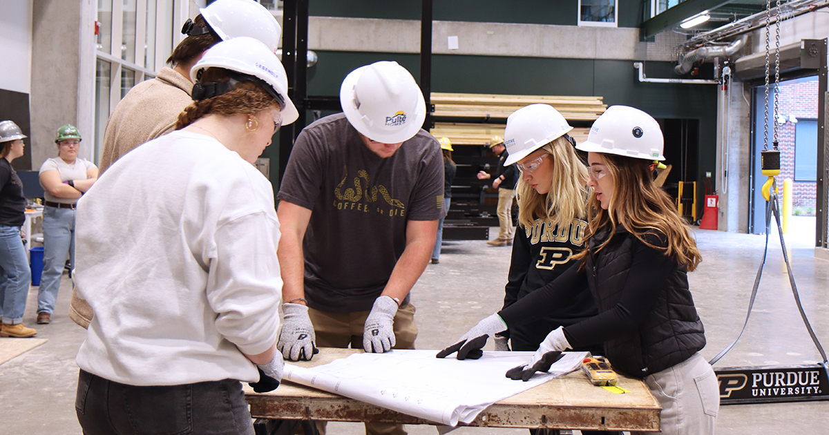 Students wear protective gear as they study blueprints standing around a table