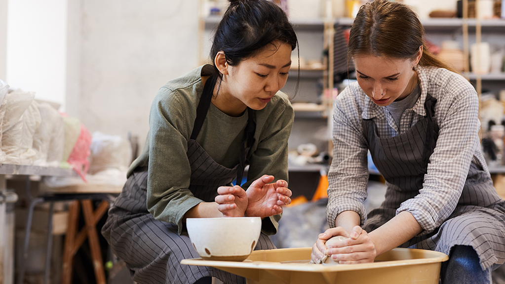 Students work together at the wheel in a ceramics studio.