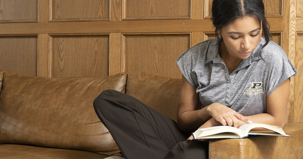 Student sits on a brown leather couch reading a book