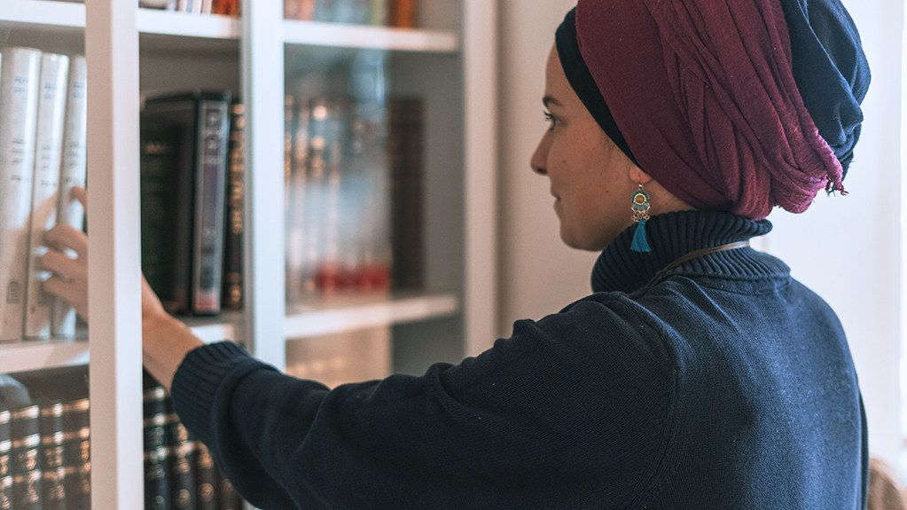 A religious Jewish woman selects a book from a bookshelf