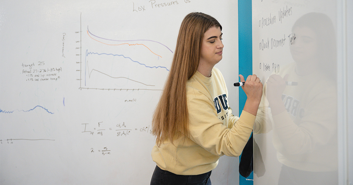student working out math problem on white board
