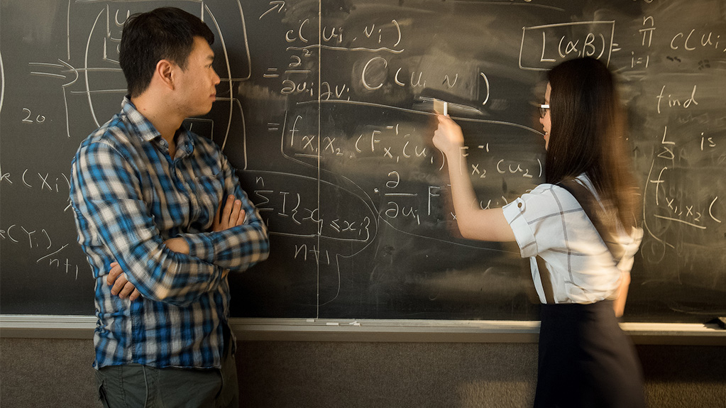 Math student working on a problem with instructor on blackboard
