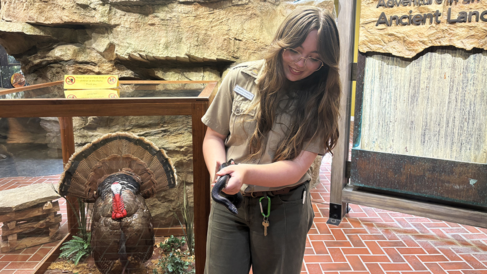 Donatella holds a snake next to a turkey exhibit