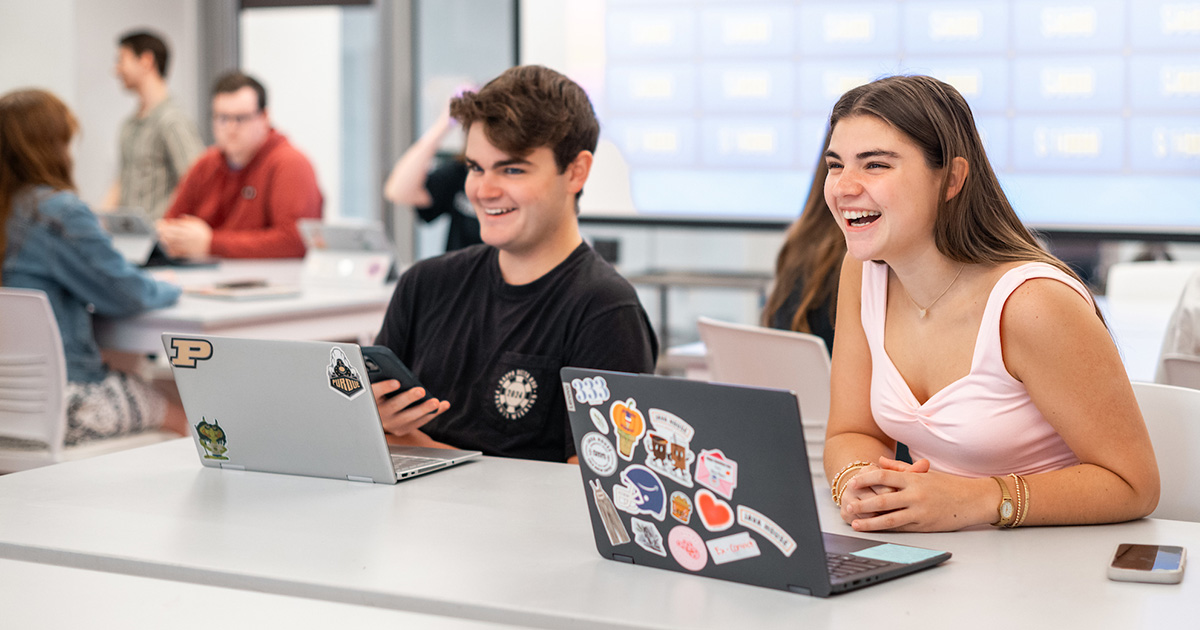 Students laughing at table with lap tops