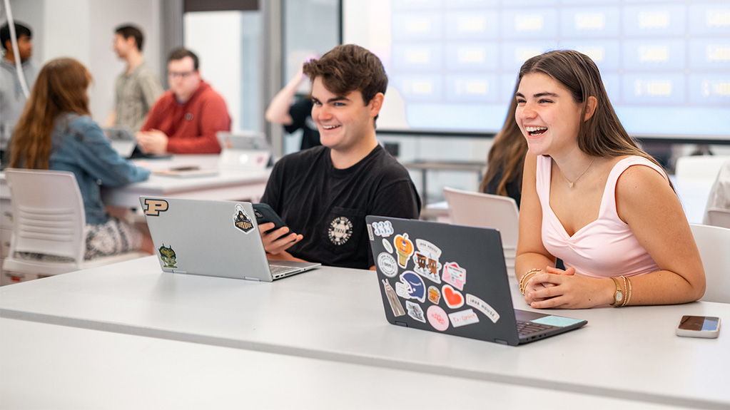 Students laughing at table with lap tops