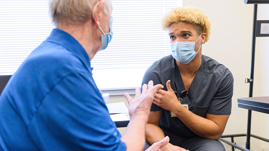 A student explains vaccine guidelines with an elderly man
