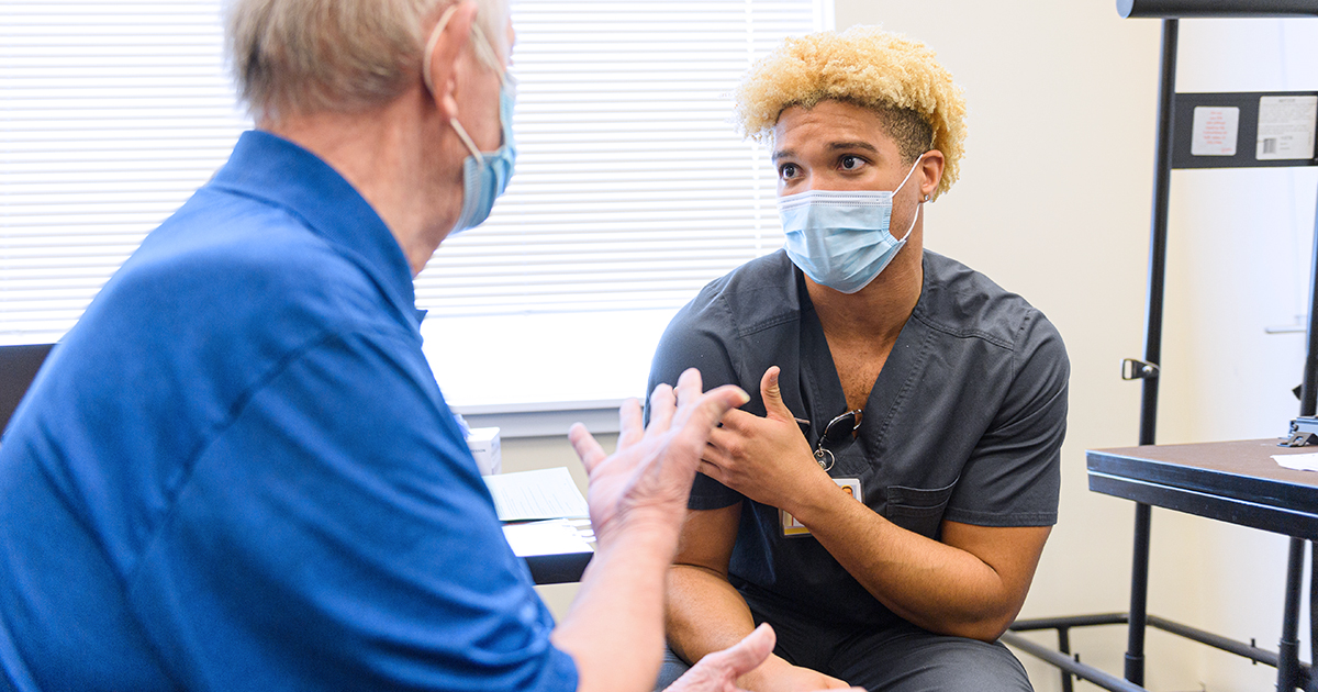 A student explains vaccine guidelines with an elderly man
