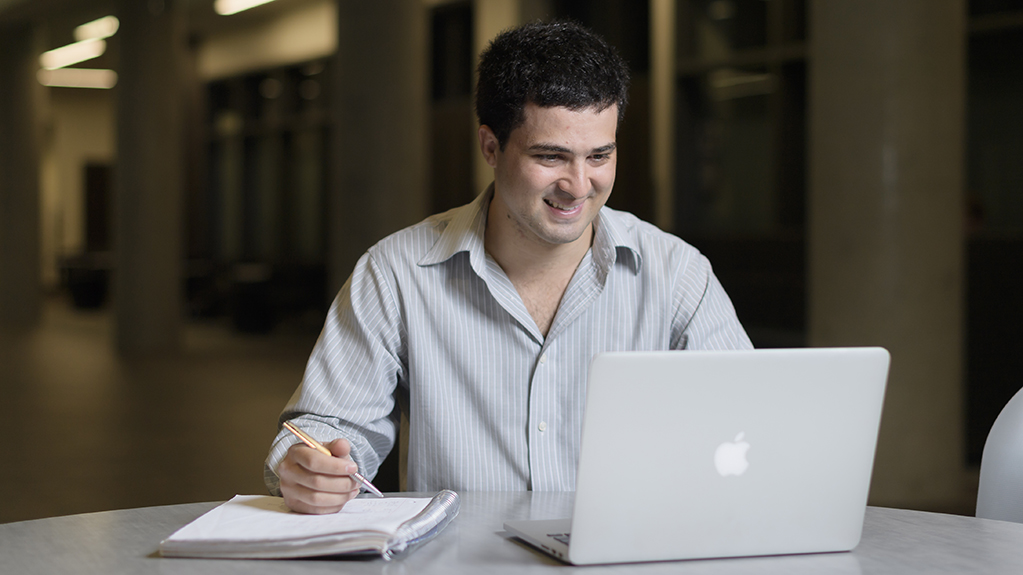 A student writes on a notebook while he looks at his laptop