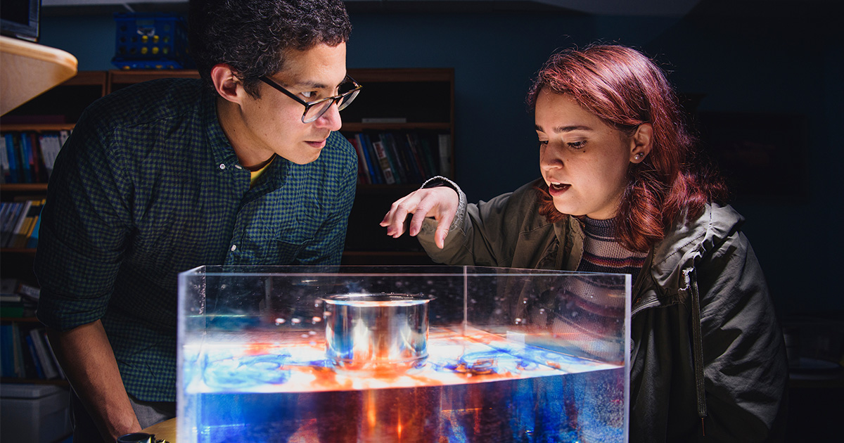 two students looking over a box of colored liquid