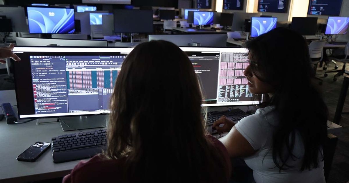 Students analyzing cybersecurity data on a large monitor in a computer lab.
