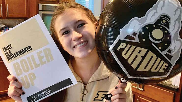 New Purdue student holding up a Purdue balloon and custom Boiler up poster.