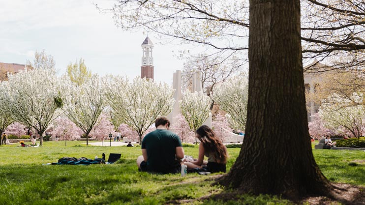 Students sitting in lawn on campus with bell tower in view.