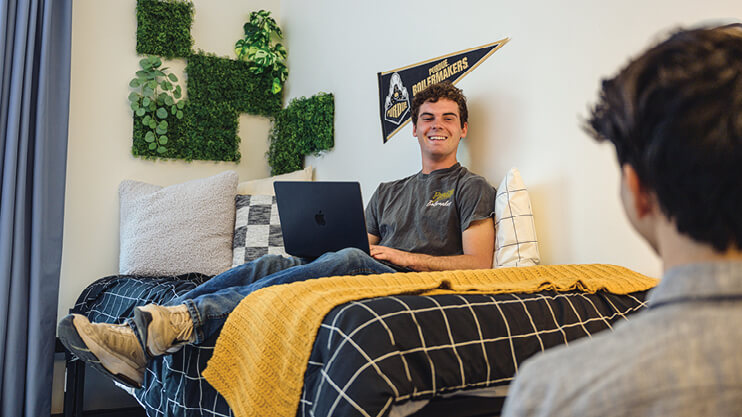 Student sitting on bed with laptop.
