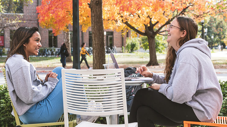 Students laughing while sitting at table outside.