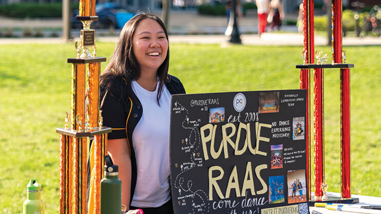 Student outside standing behind a table with large trophies on it.