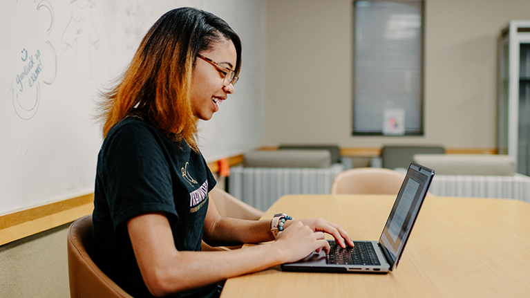 A student smiles as she works on her laptop in a classroom
