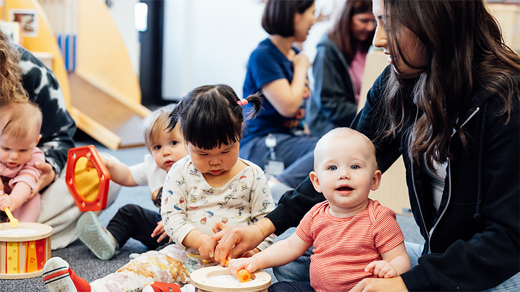 A student sits on the floor playing with infants