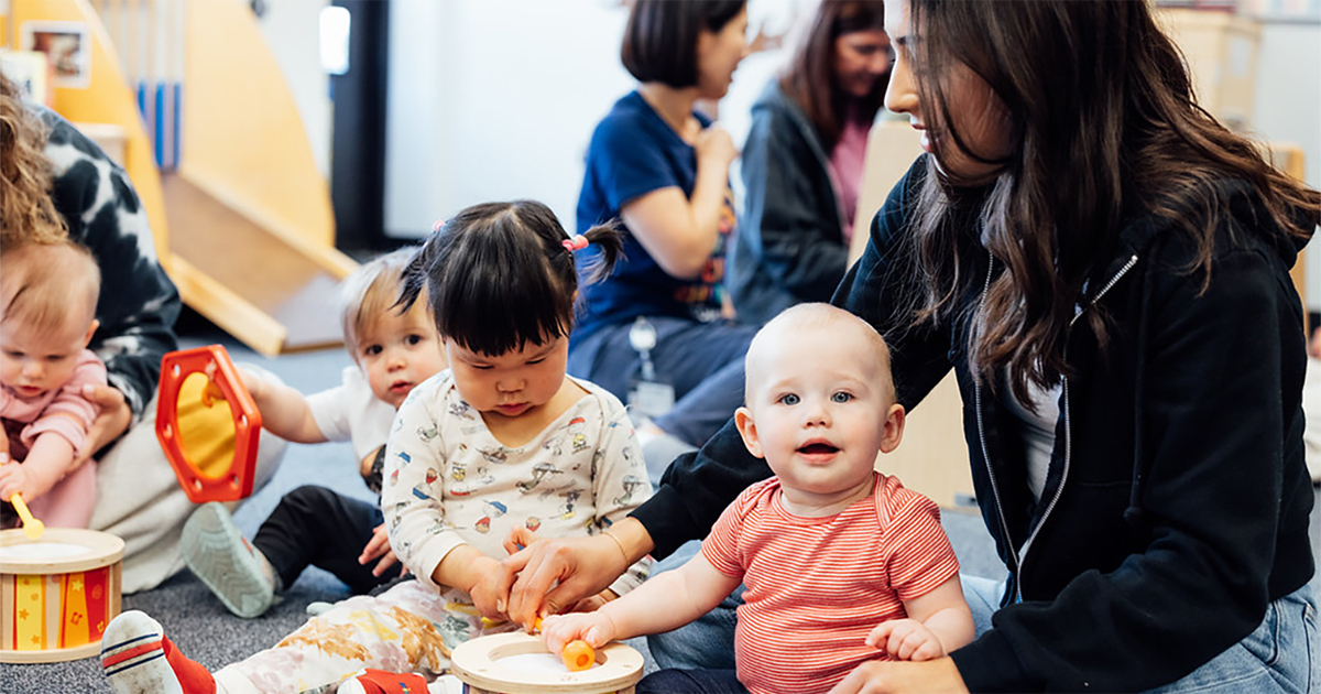 A student sits on the floor playing with infants