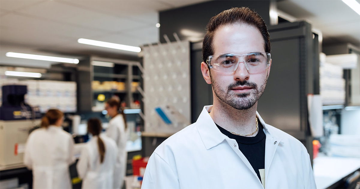 A male student stands in a lab wearing protective gear