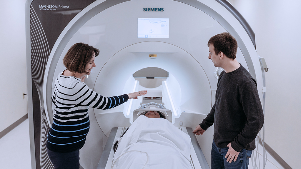 An instructor talks with a student as a patient enters an MRI machine
