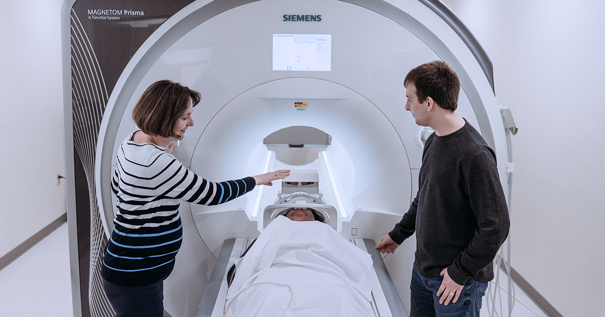 An instructor talks with a student as a patient enters an MRI machine
