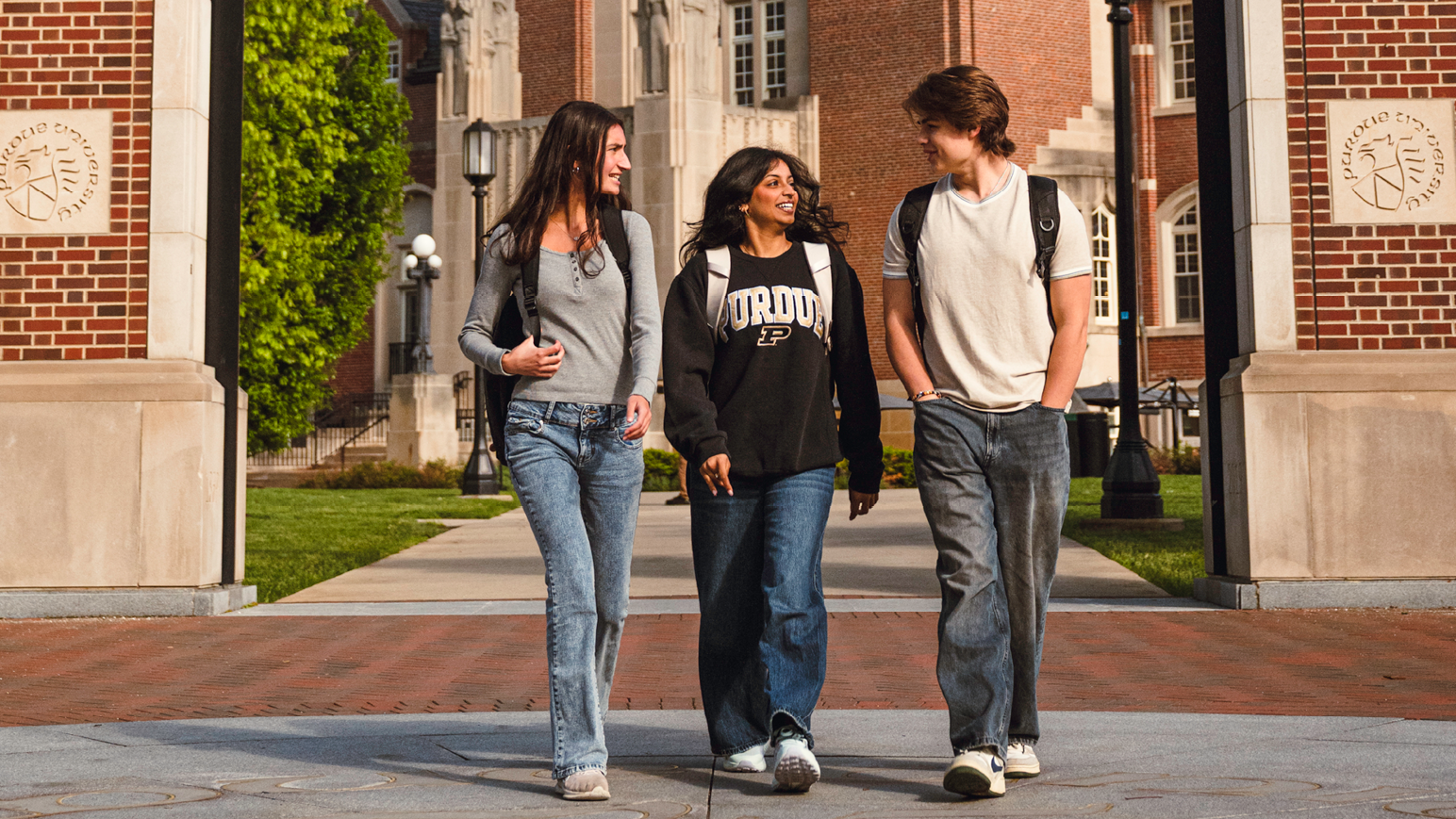 three students walk over the campus seal in front of the Purdue Memorial Union and arch