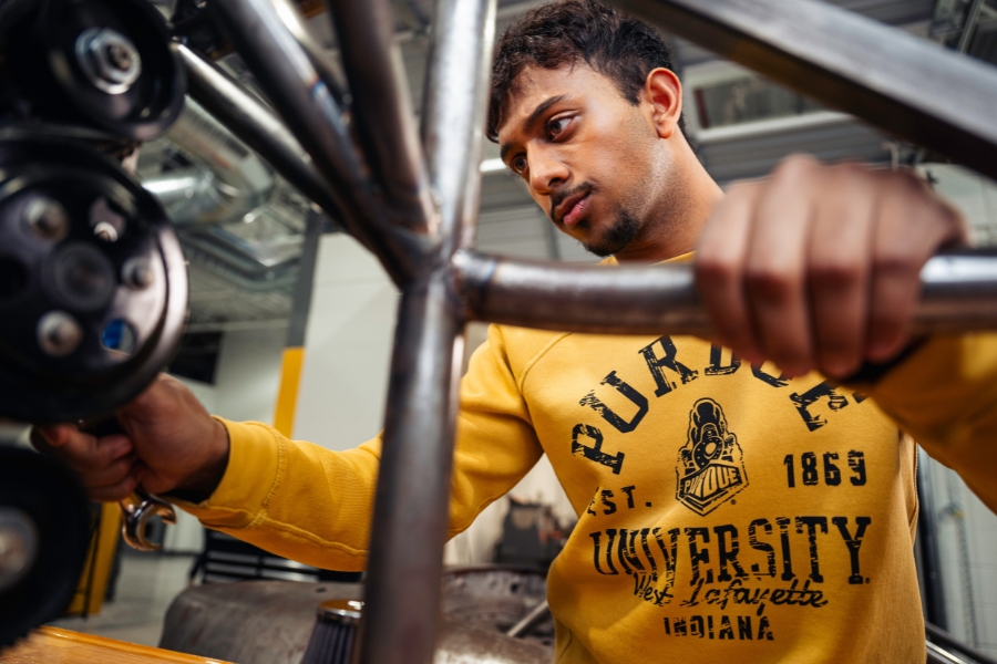 Male student wearing yellow Purdue shirt working on equipment.