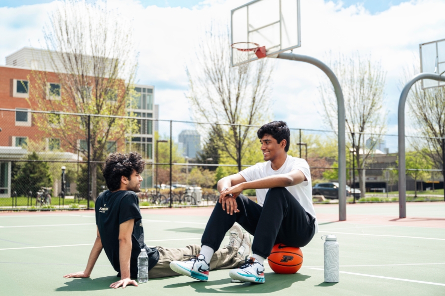 Two students sitting on basketball court facing each other.
