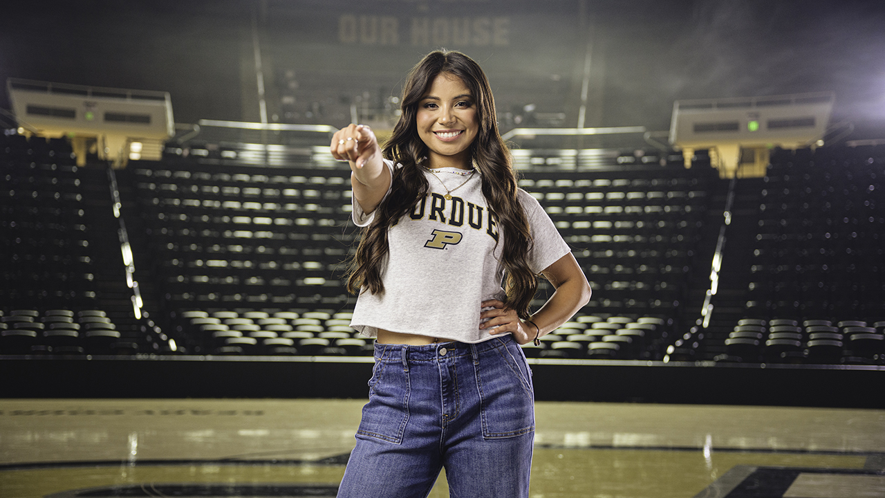 A student stands in the middle of Mackey Arena pointing toward the camera smiling with 