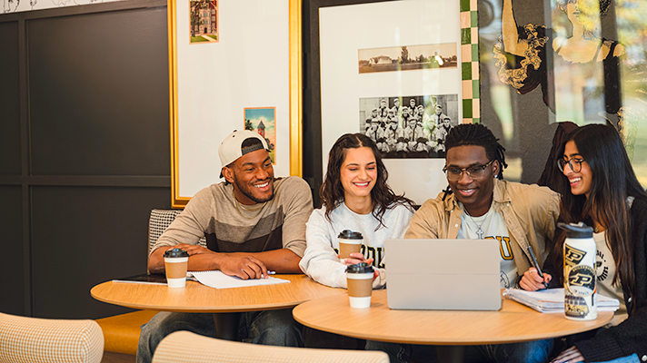 Four students sitting at a table looking at a laptop