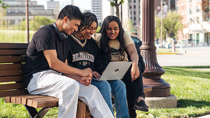 student and guardians sitting on a bench looking at a laptop together