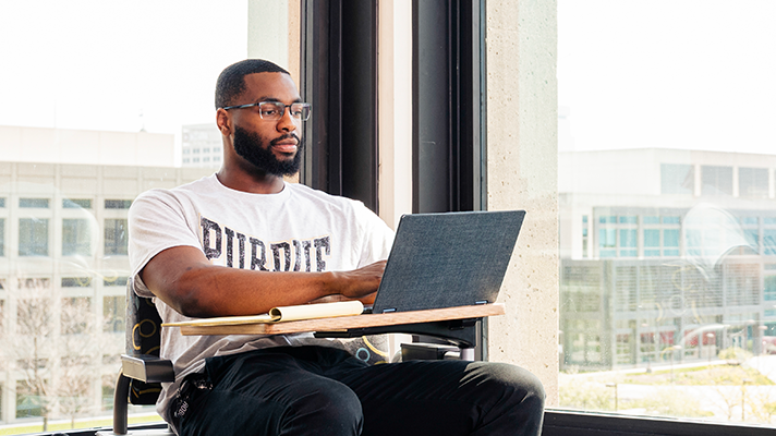Student sitting in front of windows looking at a laptop